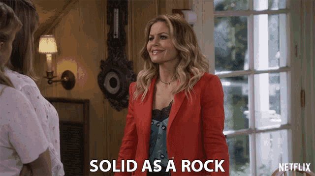 a woman in a red jacket with the words solid as a rock written below her