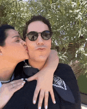 a woman is kissing a man on the cheek while he wears sunglasses