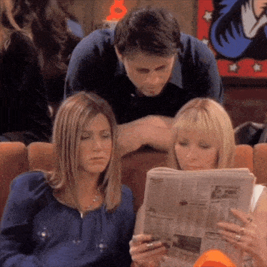 a man and two women are sitting on a couch reading a newspaper together