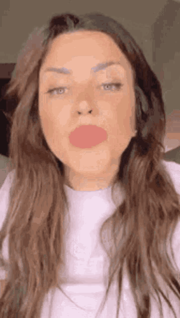 a woman with long hair is blowing a kiss while wearing a white t-shirt .