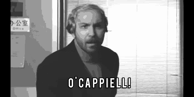 a man with a beard is standing in front of a window and says o ' cappielle