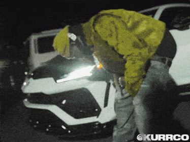 a man in a yellow jacket is standing next to a white car with the hashtag @kurrco