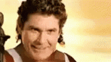 a man with curly hair is smiling and looking at the camera with a statue in the background .