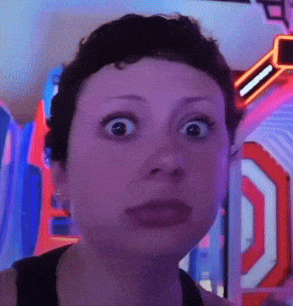 a woman with short hair is making a funny face while standing in front of a neon sign .