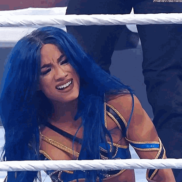 a woman with blue hair is sitting in a wrestling ring smiling