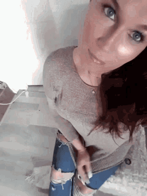 a woman wearing ripped jeans and a sweater is kneeling down on the floor .