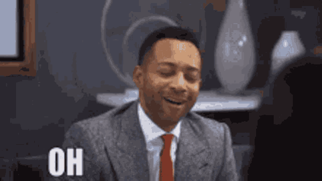 a man in a suit and tie is laughing with his eyes closed and saying oh .