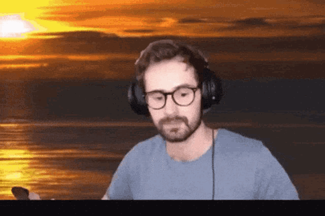 a man wearing glasses and headphones is standing in front of a sunset over the ocean