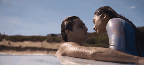 a man and a woman laying on a surfboard in the water