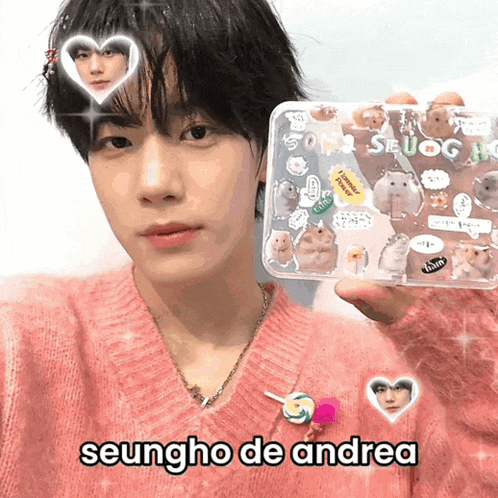 a young man in a pink sweater holds a clear case with hamsters on it