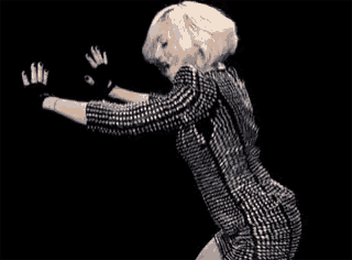a woman in a silver dress and black gloves is dancing in a dark room .