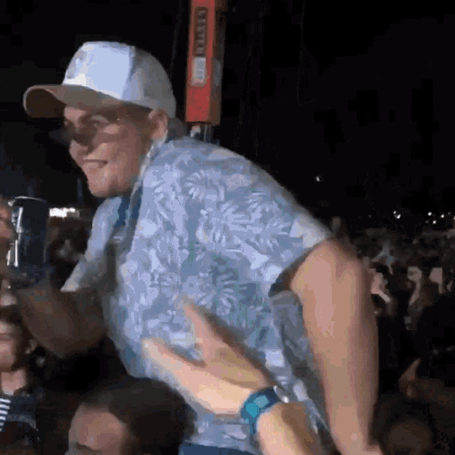 a man wearing a blue shirt and a white hat is dancing in a crowd at a concert