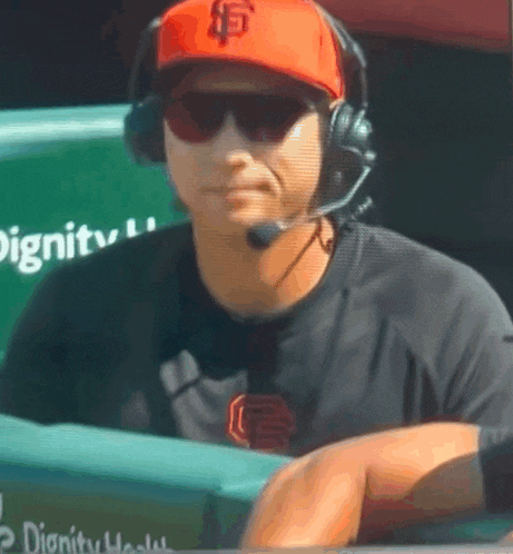 a man wearing a sf hat and headphones is sitting in the dugout