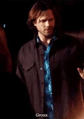 a man in a plaid shirt and a black jacket is standing in the dark and talking to a woman .