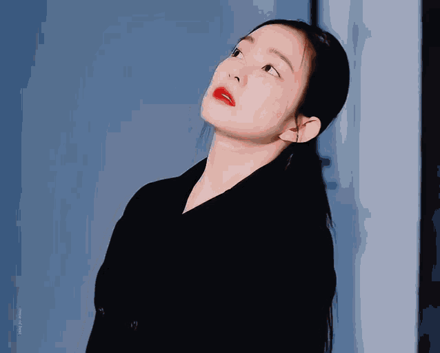 a close up of a woman wearing a black jacket and red lipstick looking up .