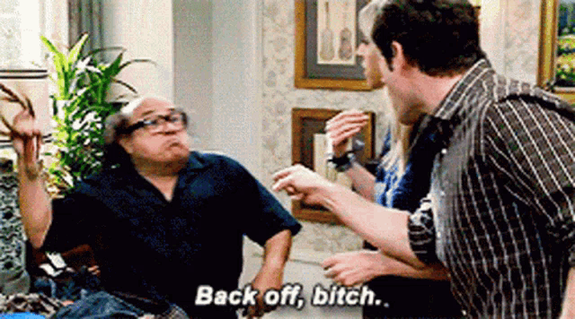a man is sitting on a couch talking to another man while another man says `` back off , bitch '' .