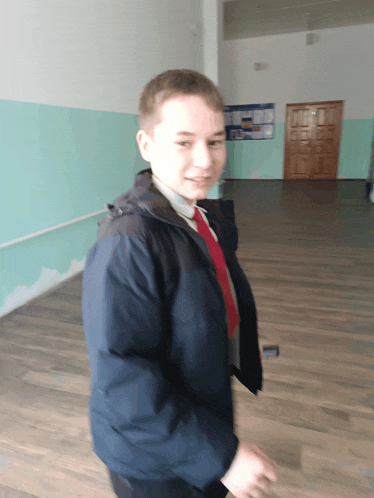 a young man in a blue jacket and red tie stands in a hallway