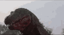 a close up of a dinosaur 's head with its mouth open and trees in the background .