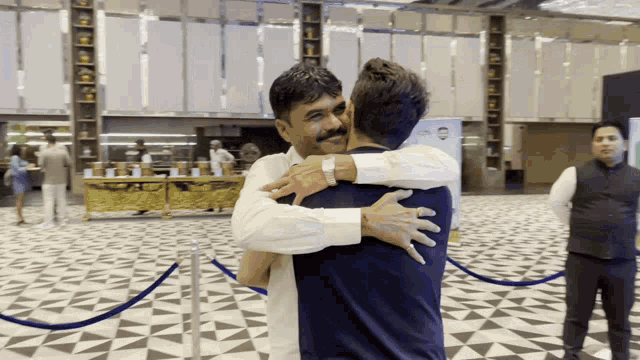 two men hugging in a room with a blue rope barrier