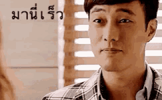 a man in a plaid shirt is looking at the camera with a foreign language behind him .