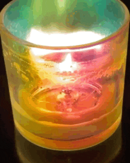 a candle in a glass with a rainbow colored background