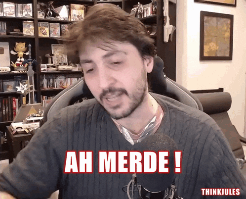 a man sitting in front of a microphone with the words ah merde written in red