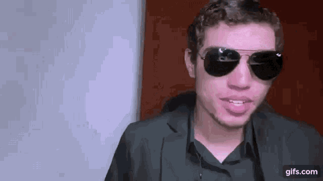 a man wearing sunglasses and a suit is smiling and making a funny face .