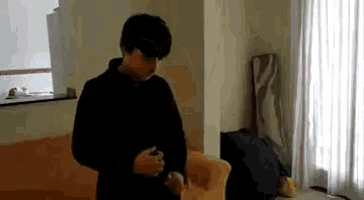 a man in a black sweater is standing in a living room next to an orange couch .