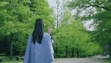 a woman in a blue cape stands in a park surrounded by green trees