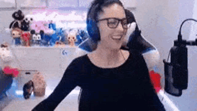 a woman wearing headphones and glasses is standing in front of a microphone .