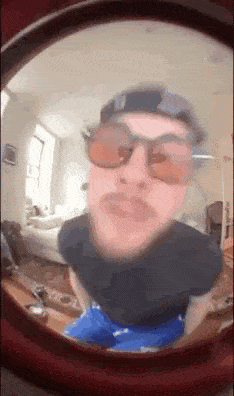 a man wearing sunglasses and a baseball cap is taking a selfie in a room .