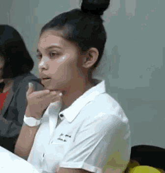 a young woman in a white shirt is sitting in a classroom with other students .