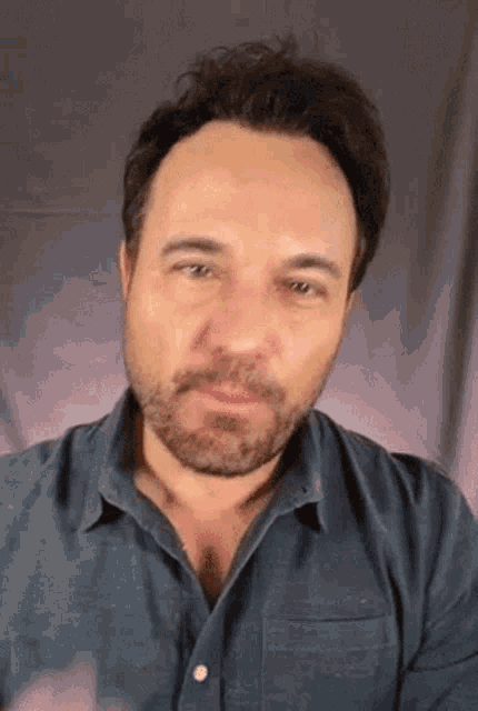 a man with a beard is wearing a blue shirt and making a funny face .
