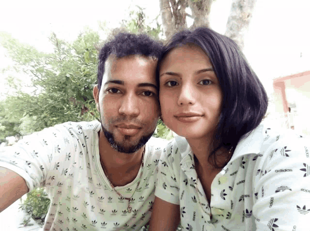 a man and a woman are posing for a picture and the woman is wearing a white adidas shirt