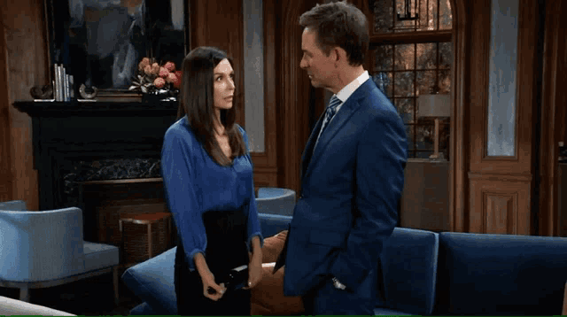 a man in a suit and tie stands next to a woman in a blue top