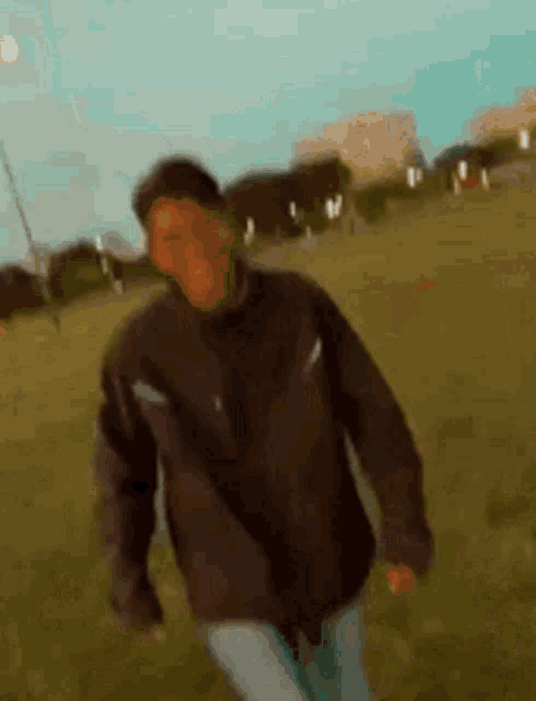 a blurry picture of a man in a black jacket walking in a field .
