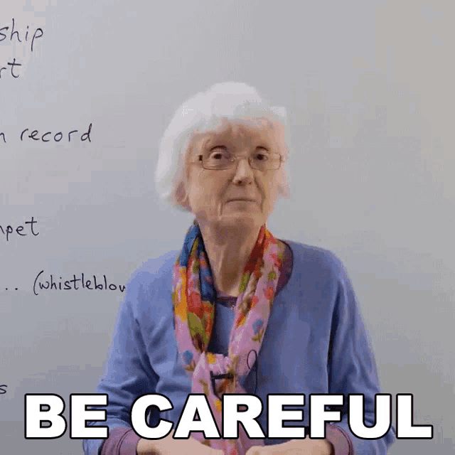 an elderly woman says " be careful " in front of a white board