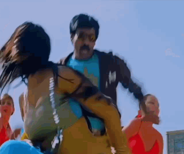a man is carrying a woman on his shoulders while a group of people are dancing .