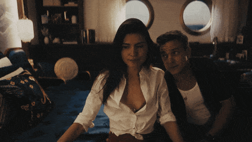 a man and a woman are sitting on a couch and the woman 's shirt is open