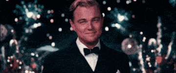 a man in a tuxedo and bow tie smiles in front of fireworks