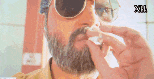 a man with a beard wearing sunglasses is smoking a cigarette with the letters xh on the bottom left