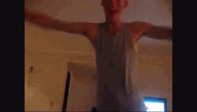 a man in a tank top stands in front of a tv