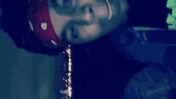 a man wearing a bandana and a necklace is laying down in a dark room .