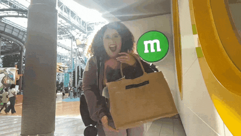 a woman holds a bag in front of a green m & m sign