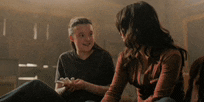 two women are sitting on the floor holding hands and talking .