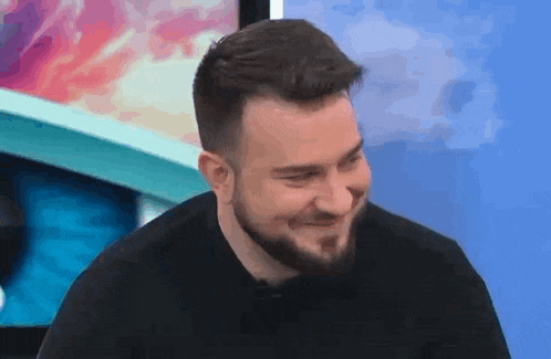 a man with a beard is smiling and laughing while sitting in front of a television .