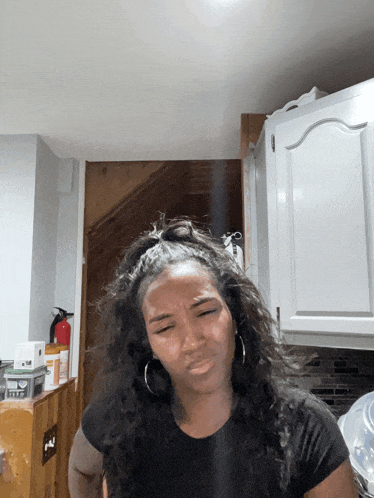 a woman making a funny face in a kitchen with white cabinets