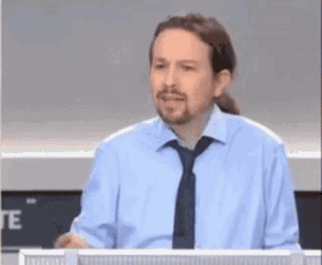 a man in a light blue shirt and tie is standing in front of a computer screen .