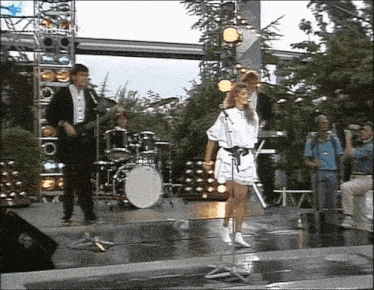 a woman in a white dress sings into a microphone in front of a band