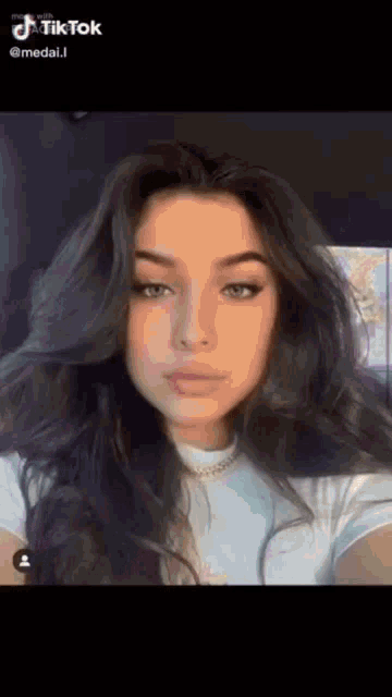 a woman with long dark hair is taking a selfie with her phone .